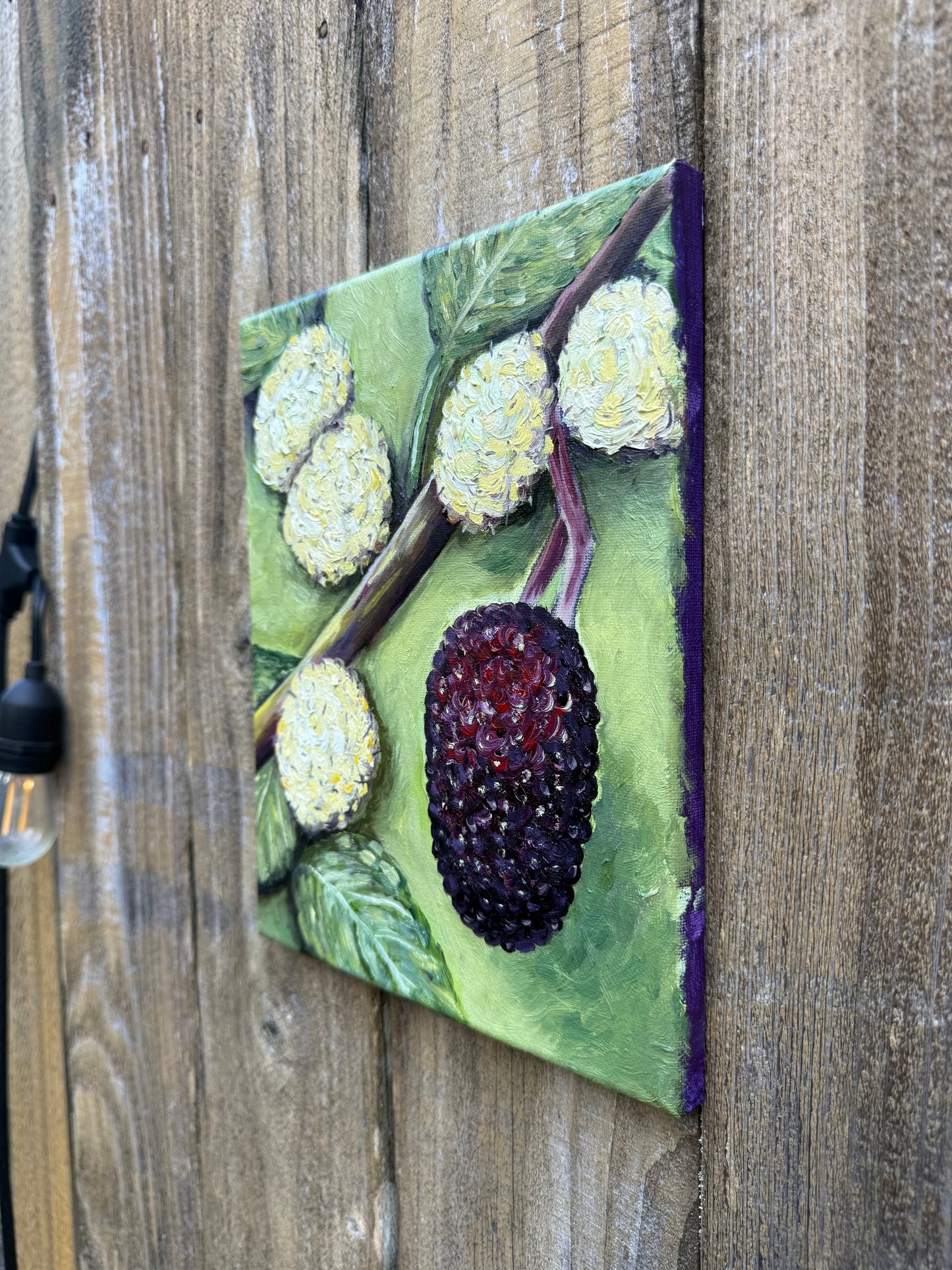 oil painting with mulberries that look like blackberries and green leaves on a wooden surface
